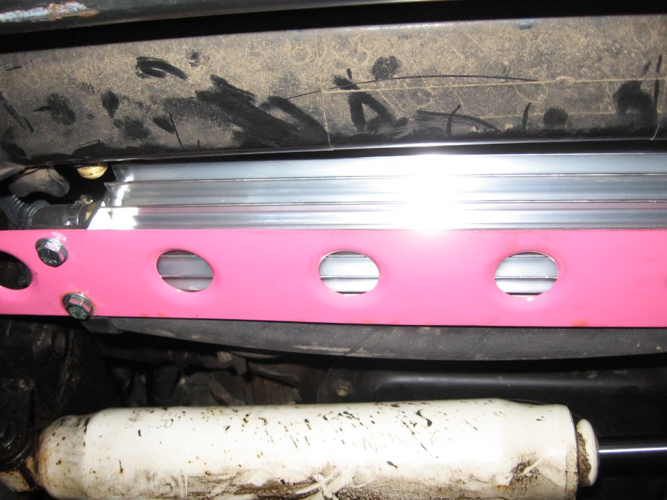 Pink strut bar with circular cutouts above a dirty white shock absorber