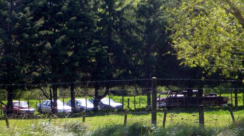 1969 Lincoln Continental - An old car, possibly a convertible with its roof removed, sits abandoned in a grassy field behind a fence.