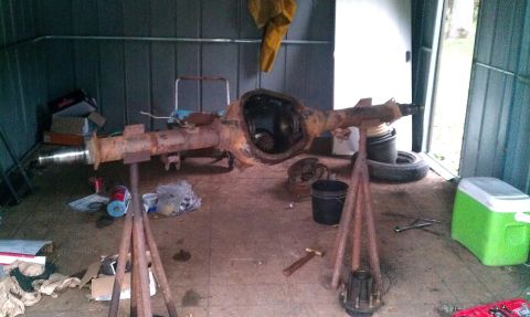 1995 Ford Bronco - A rusty rear axle assembly is supported on stands inside a shed, with tools and supplies scattered around.