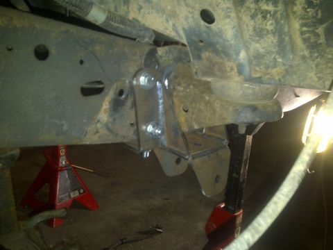 1995 Ford Bronco - Custom suspension bracketry is welded to the frame of a vehicle, which is supported by red jack stands.
