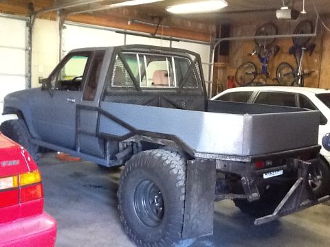 1988 Suzuki Samurai - A modified truck with a flatbed and roll cage sits in a garage, with another vehicle partially visible.