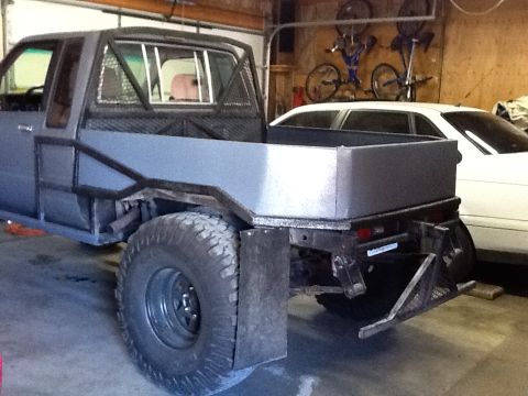 1988 Suzuki Samurai - A modified truck with a flatbed and roll cage sits in a garage, with another vehicle visible behind it.