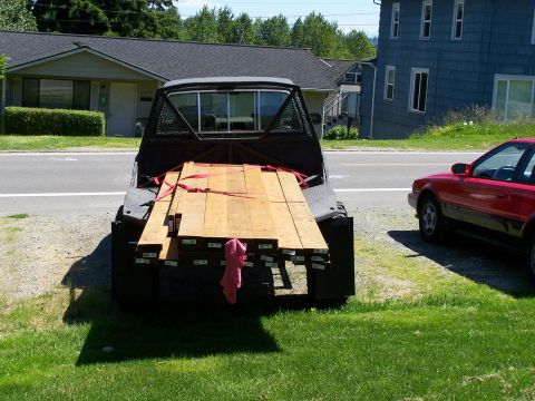 1988 Suzuki Samurai - A pickup truck bed is filled with lumber, parked next to a red car.