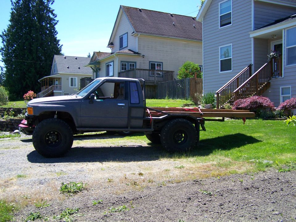 Modified pickup truck with flatbed and large tires, parked on gravel and grass