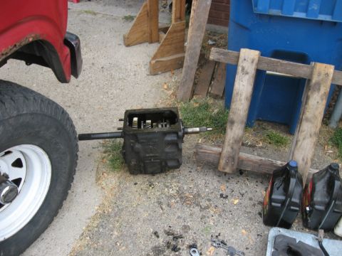 1981 Ford Bronco - Transmission removed from vehicle, with parts and fluids on the ground.