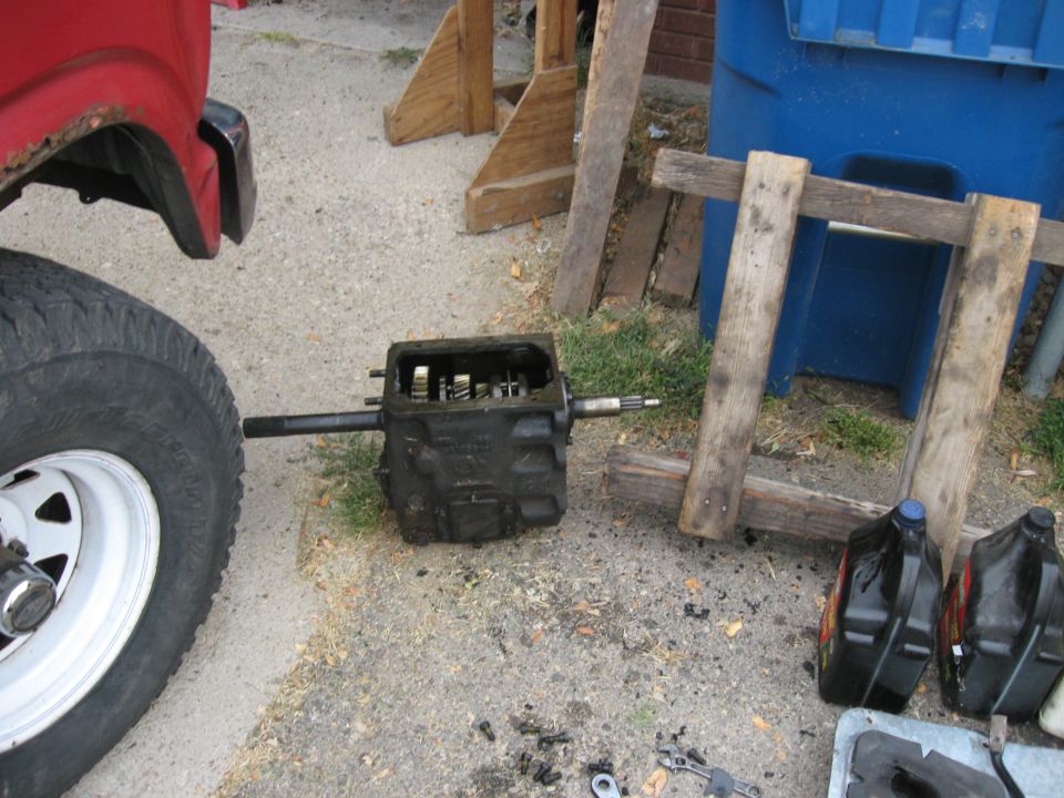 Removed transmission and loose parts on the ground next to a red vehicle's tire