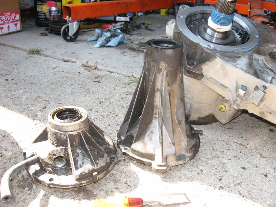 two greasy transmission housings sit on concrete next to a larger transmission assembly