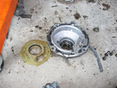 1981 Ford Bronco - Disassembled transmission housing and adapter plate on a concrete floor with oil stains.