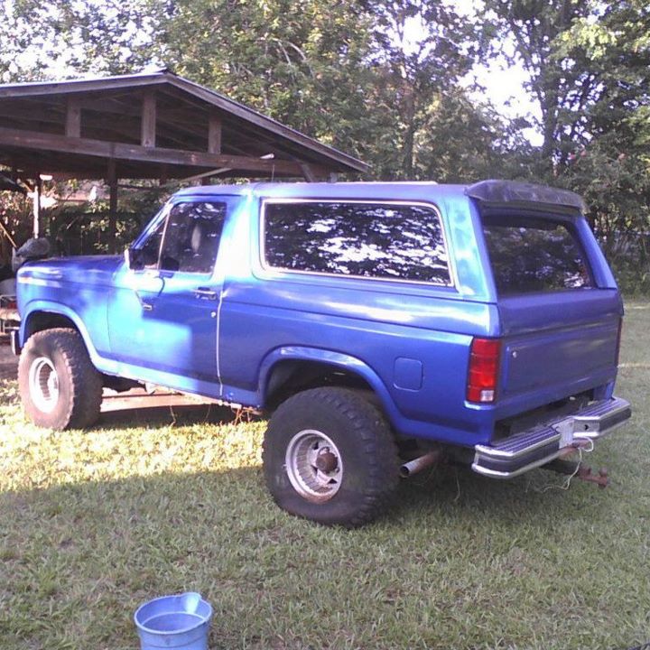 Blue Ford Bronco parked on grass next to a wooden shelter