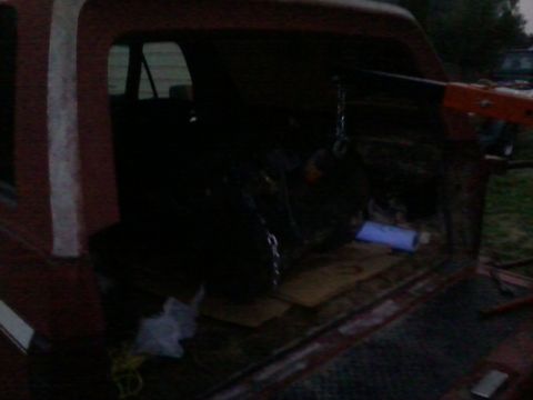 1981 Ford Bronco - An engine is being loaded into the cargo area of a red truck, likely for an engine swap.