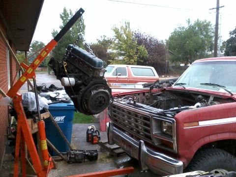 1981 Ford Bronco - An engine is being removed from a red truck with an engine hoist. A second vehicle is visible in the background.