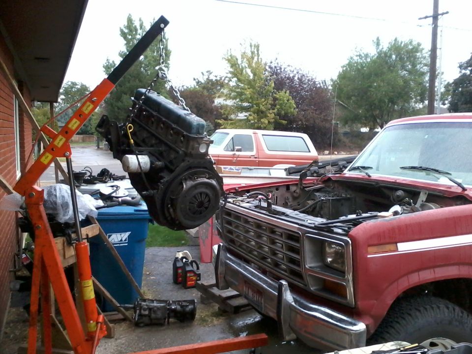 Engine hoist lifting an engine out of a red truck. Another SUV is parked behind it