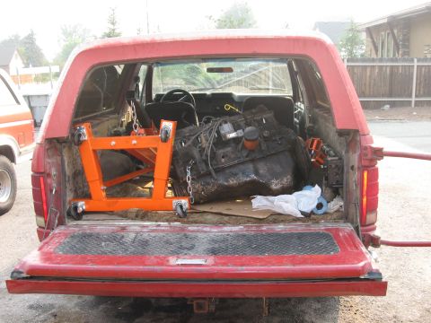 1981 Ford Bronco - A red SUV's open tailgate reveals an engine and engine stand, with another vehicle visible to the side.