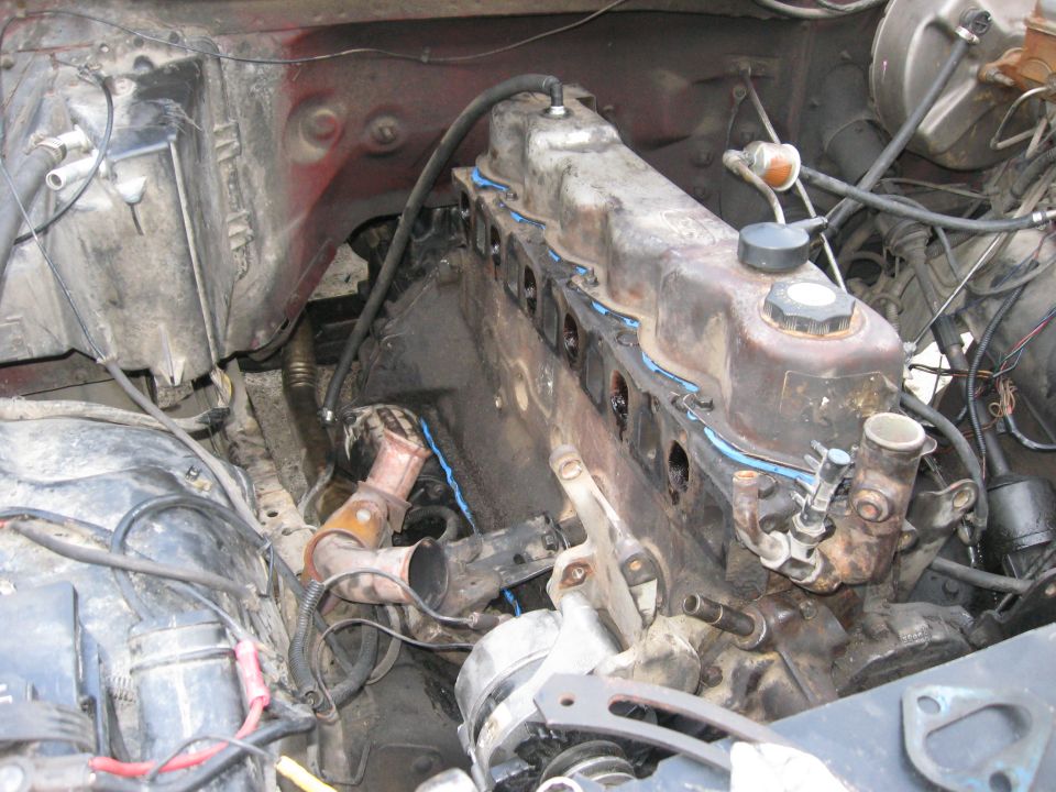 Engine bay showing a V8 engine block, cylinder heads, exhaust manifold, and alternator. Some hoses and wiring are visible