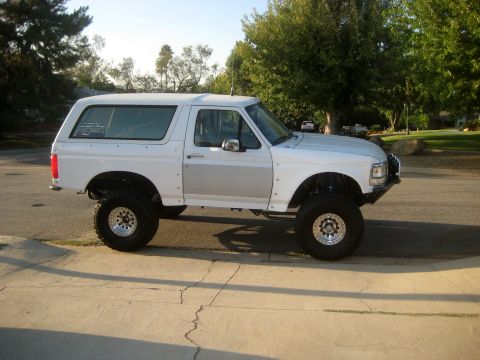 1996 Ford Bronco - Modified white Ford Bronco with large tires and custom fender flares sits on a street.