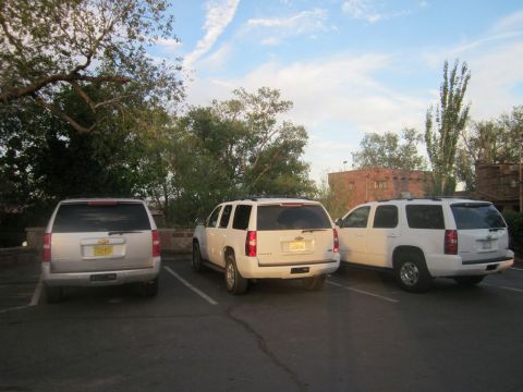 1991 Ford LTD Crown Victoria - Three Chevrolet Suburbans are parked in a lot with trees and buildings in the background.