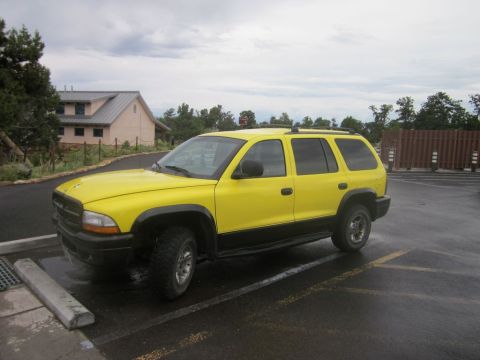 1991 Ford LTD Crown Victoria - A yellow SUV with black trim is parked in a wet lot under a cloudy sky.