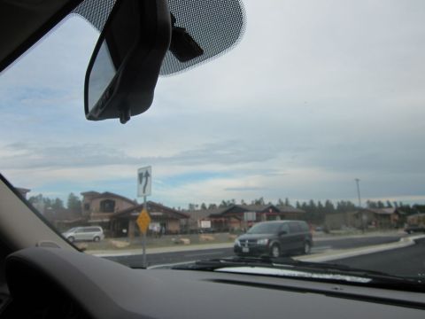 1991 Ford LTD Crown Victoria - A dark minivan is seen driving on a road, with buildings and trees in the background under a cloudy sky.