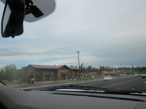 1991 Ford LTD Crown Victoria - A view from inside a vehicle shows a commercial building and a road with a white car driving under a cloudy sky.