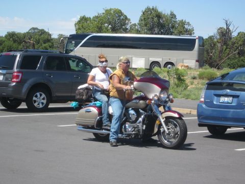 1991 Ford LTD Crown Victoria - A motorcycle carrying two people is parked in a lot with other vehicles and a tour bus.