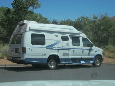 1991 Ford LTD Crown Victoria - A white and blue camper van is parked on the side of the road with trees in the background.