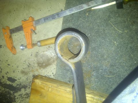 1995 Ford Bronco - A metal pipe fitting is secured by a clamp and a wooden block on a carpeted surface.
