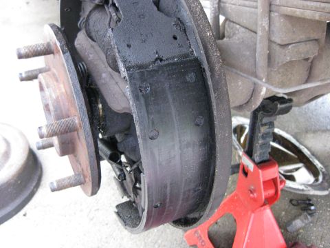 1994 Ford Bronco - Close-up of a worn brake drum and shoes on a vehicle's rear axle, with a red jack visible.