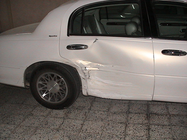 White sedan, rear passenger side has significant damage to the quarter panel and door