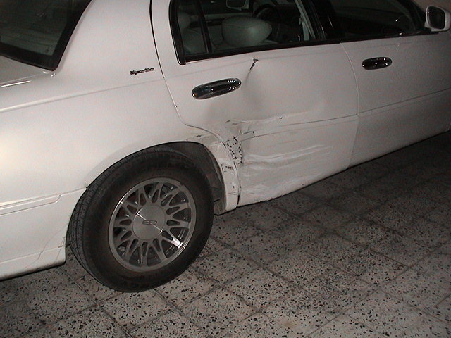 White sedan with significant rear door damage and dented quarter panel