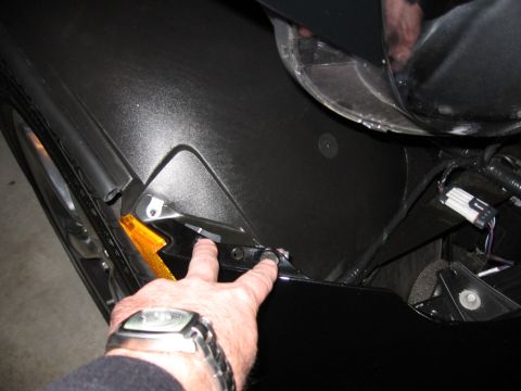 1995 Ford Bronco - A hand points to a bolt on the fender assembly of a black car, revealing the turn signal and wiring.