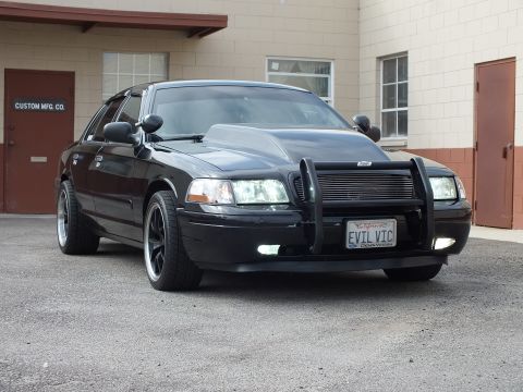 2003 Ford Crown Victoria - Glossy black Crown Victoria poses at an angle showing chrome-lip black wheels and EVIL VIC plate.