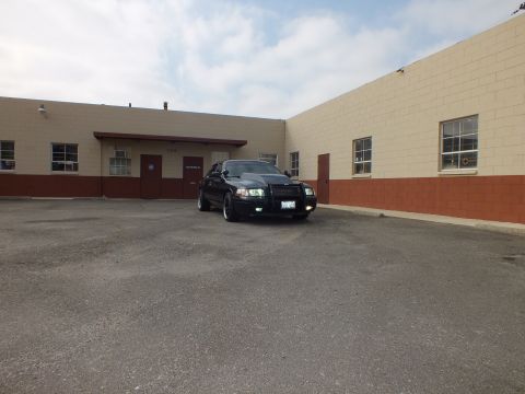 2003 Ford Crown Victoria - dark Crown Victoria sits small in frame against a long two-tone commercial wall.