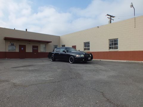 2003 Ford Crown Victoria - Wide daylight view places the dark sedan against a long commercial building and utility pole.