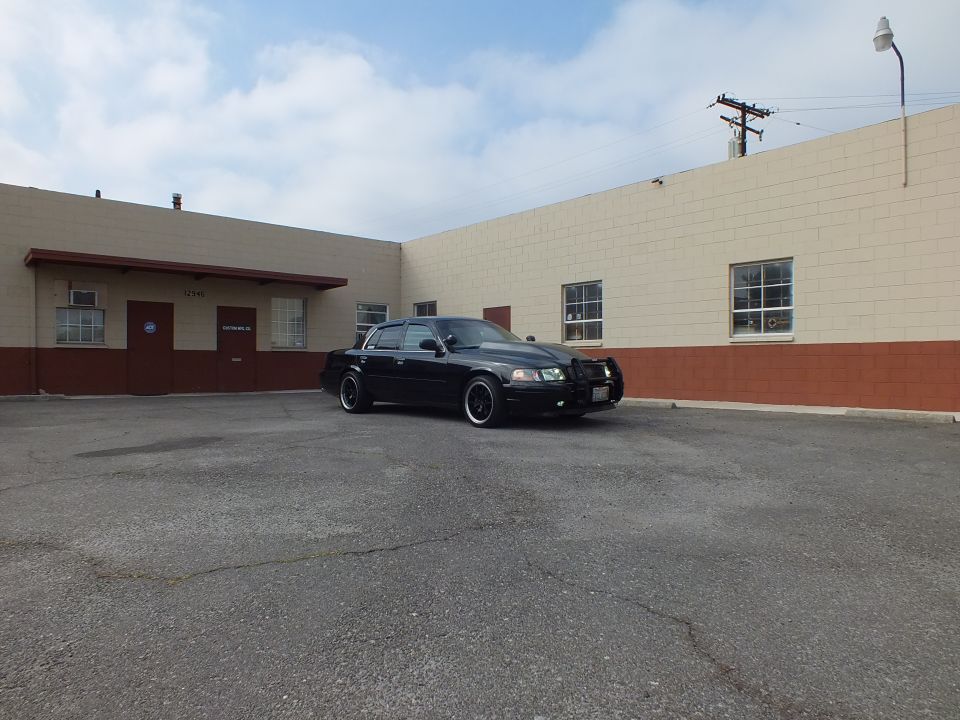 Black Crown Victoria parked beside tan building with power pole and street lamp under cloudy sky