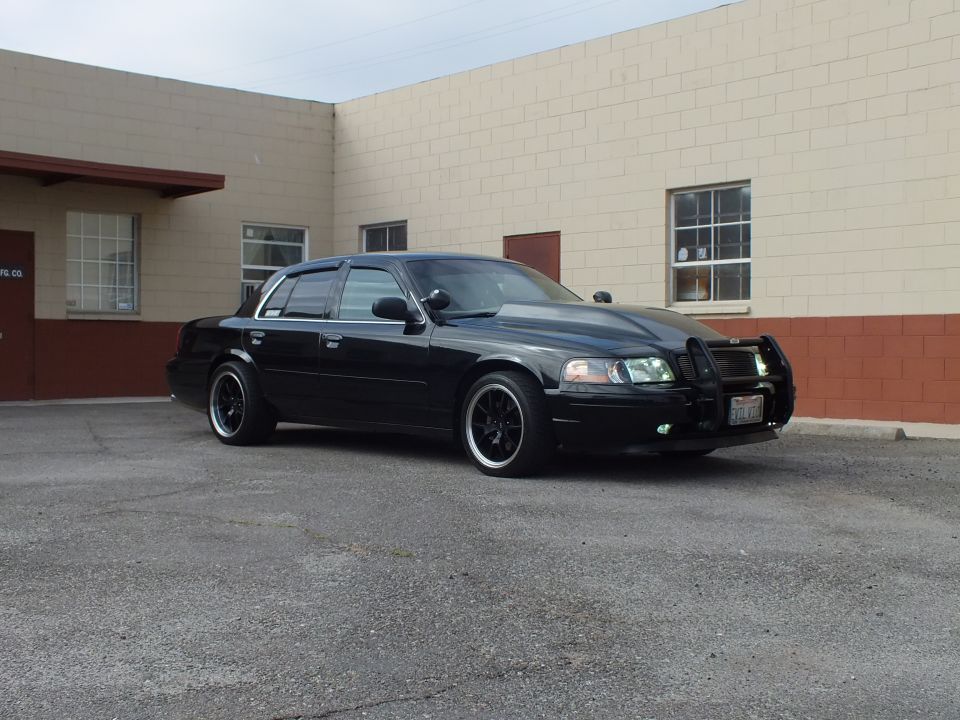 Front three-quarter of lowered black Crown Victoria with grille guard and black wheels in lot