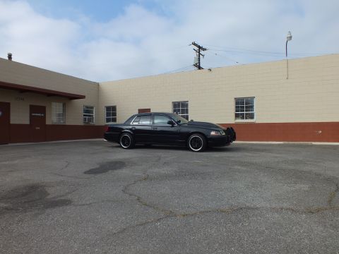 2003 Ford Crown Victoria - distant profile of the dark sedan stretched along an empty lot under cloudy sky.