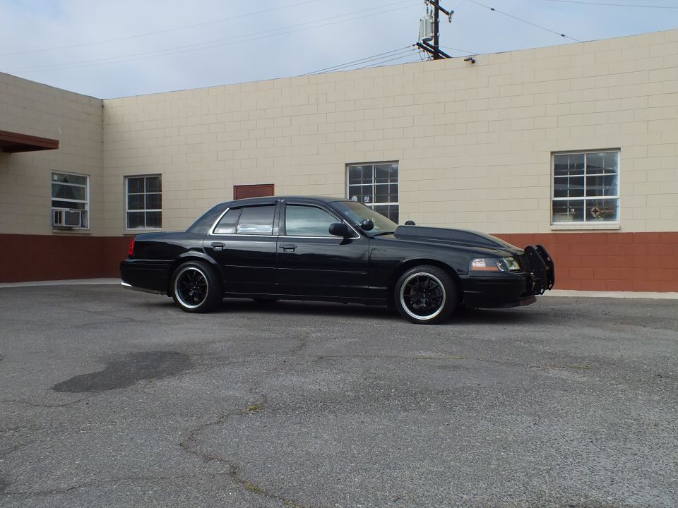 Side profile of black Ford Crown Victoria with grille guard and staggered black wheels by building