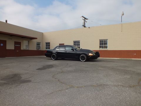 2003 Ford Crown Victoria - Wide profile view of the dark sedan parked alone in a large asphalt lot.