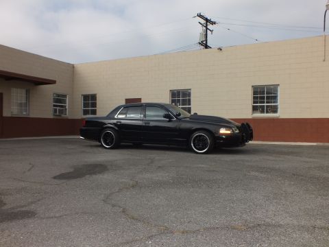 2003 Ford Crown Victoria - Crown Victoria sits side-on in a broad parking lot beneath a utility pole and cloudy sky.