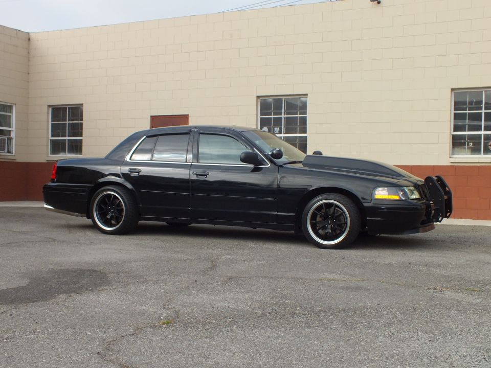 Passenger-side profile of black Crown Victoria with grille guard and staggered black wheels
