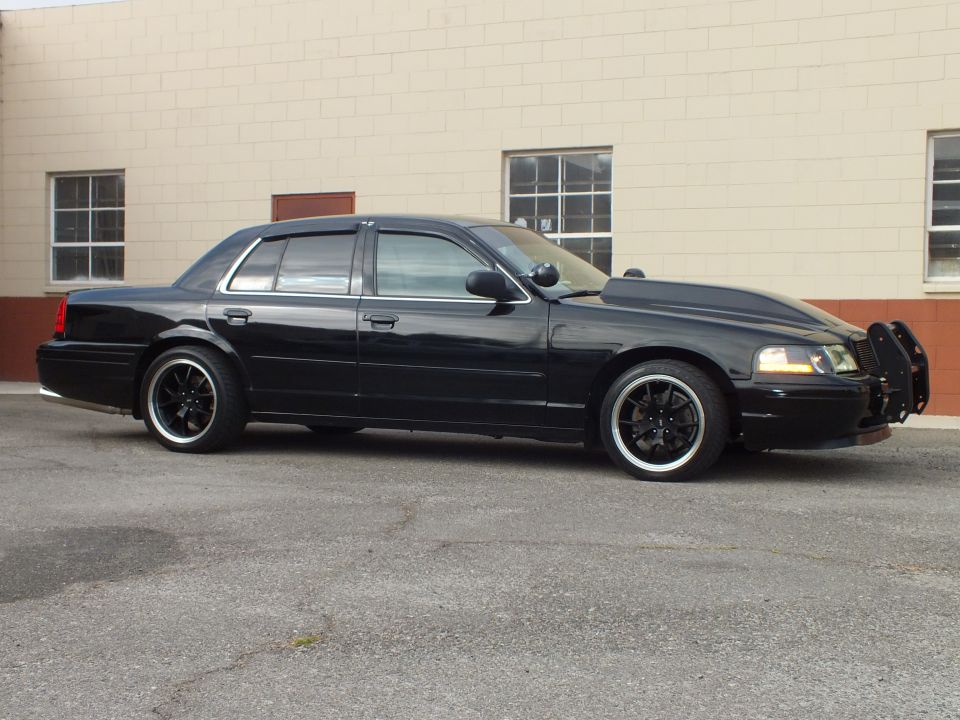 Black Ford Crown Victoria sedan, driver side, lowered on black wheels with front push bar