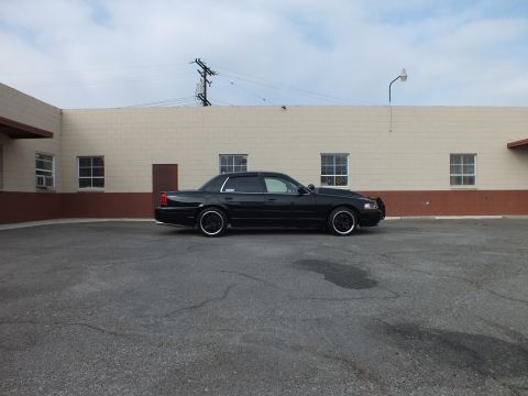 2003 Ford Crown Victoria - Lowered black sedan sits across a wide parking lot under overhead power lines and a streetlight.