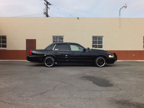 2003 Ford Crown Victoria - Passenger-side view of a blacked-out Crown Victoria with chrome rocker trim beside a brick wall.
