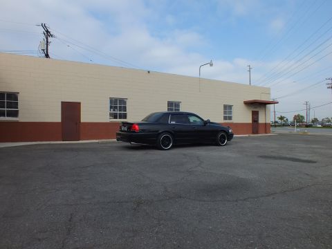 2003 Ford Crown Victoria - Lowered black sedan photographed from the rear corner across an empty lot under power lines.