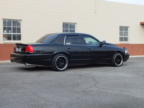 2003 Ford Crown Victoria - Rear passenger angle of a blacked-out sedan with trunk spoiler and chrome rocker trim.
