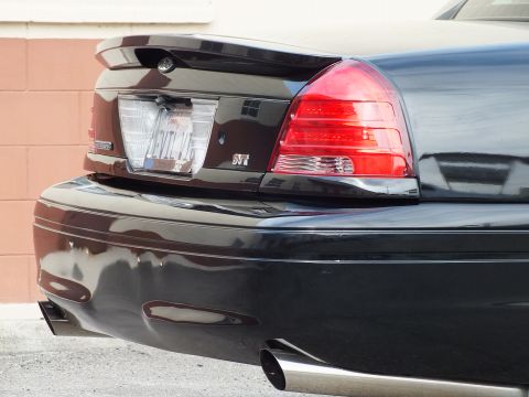 2003 Ford Crown Victoria - Detail of a black sedan's rear corner showing the SVT trunk badge, red taillight and dual exhaust.