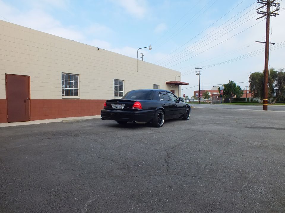 Black Ford Crown Victoria sedan, rear view in empty lot beside tan industrial building