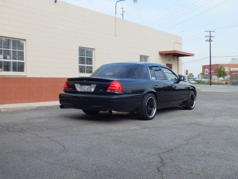 2003 Ford Crown Victoria - Rear three-quarter of a black sedan with trunk spoiler and EVIL VIC plate near a stop sign.