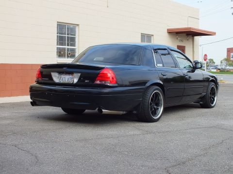 2003 Ford Crown Victoria - Rear corner of a blacked-out sedan showing the EVIL VIC plate, SVT badge and black wheels.