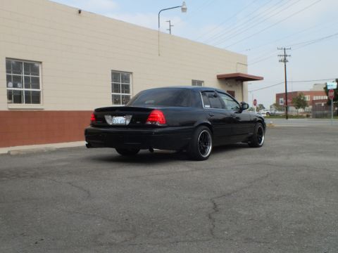 2003 Ford Crown Victoria - Rear quarter view of a lowered black Crown Victoria sedan on black aftermarket wheels in an empty lot